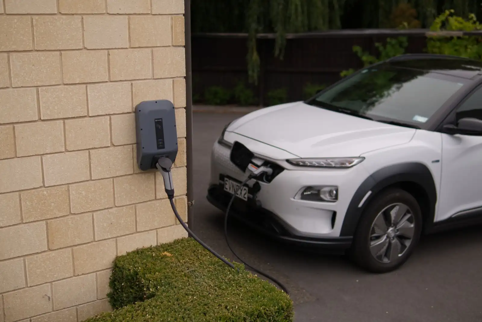 Electric car charging from a wall-mounted home charger on a driveway